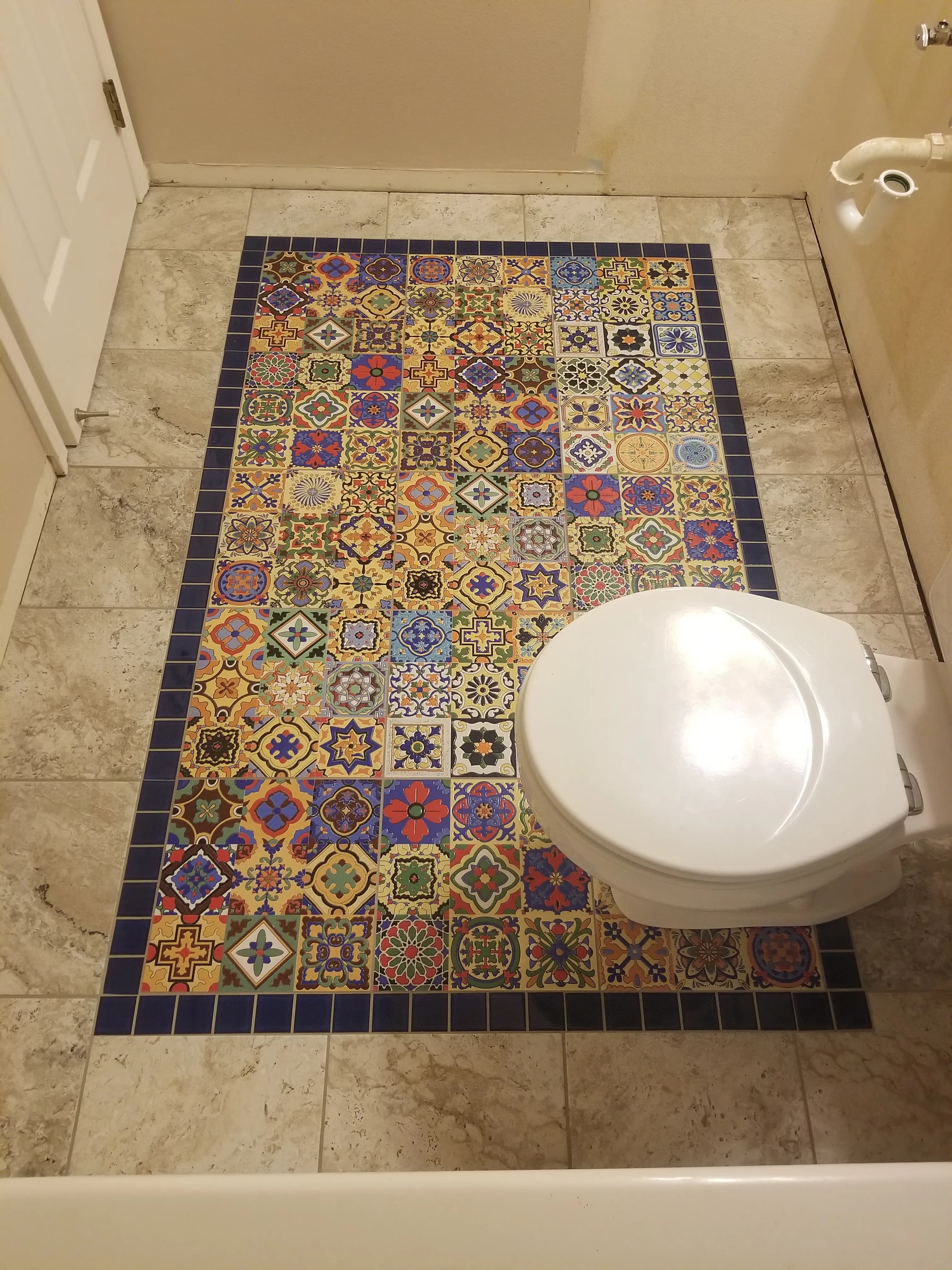 Colorful patterned tile rug inset bordered by neutral floor tile in a small entry area
