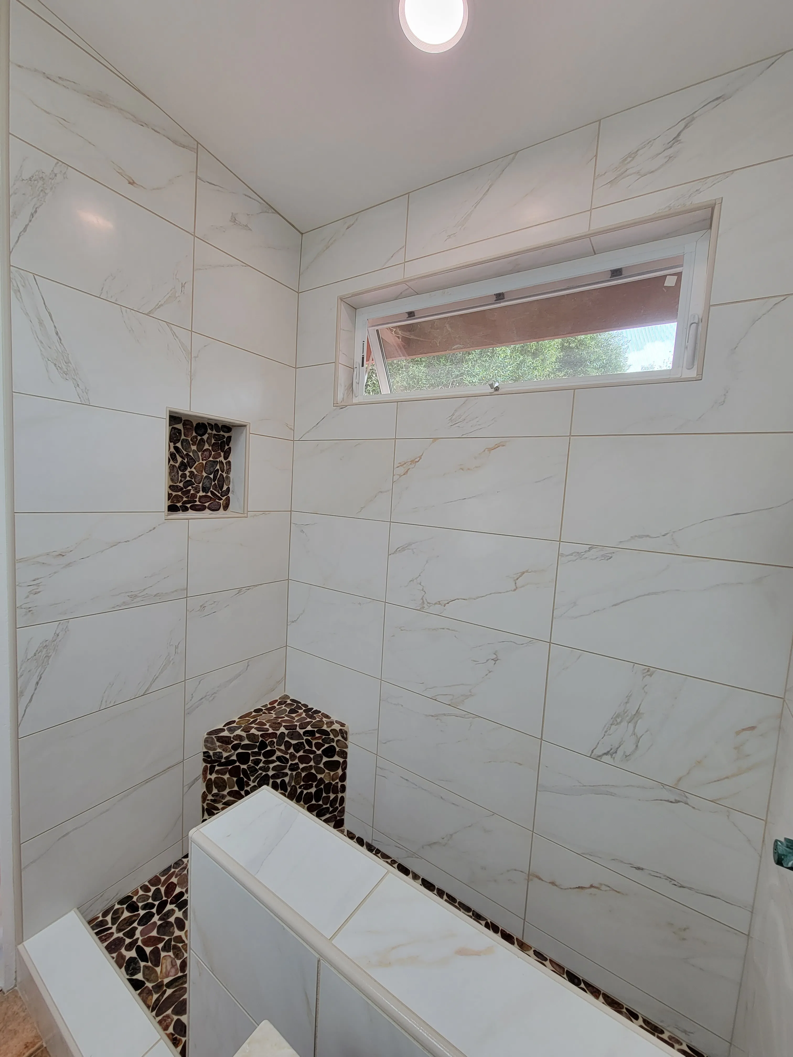 Walk-in shower with large marble-look tiles, horizontal window, and pebble mosaic niche accents