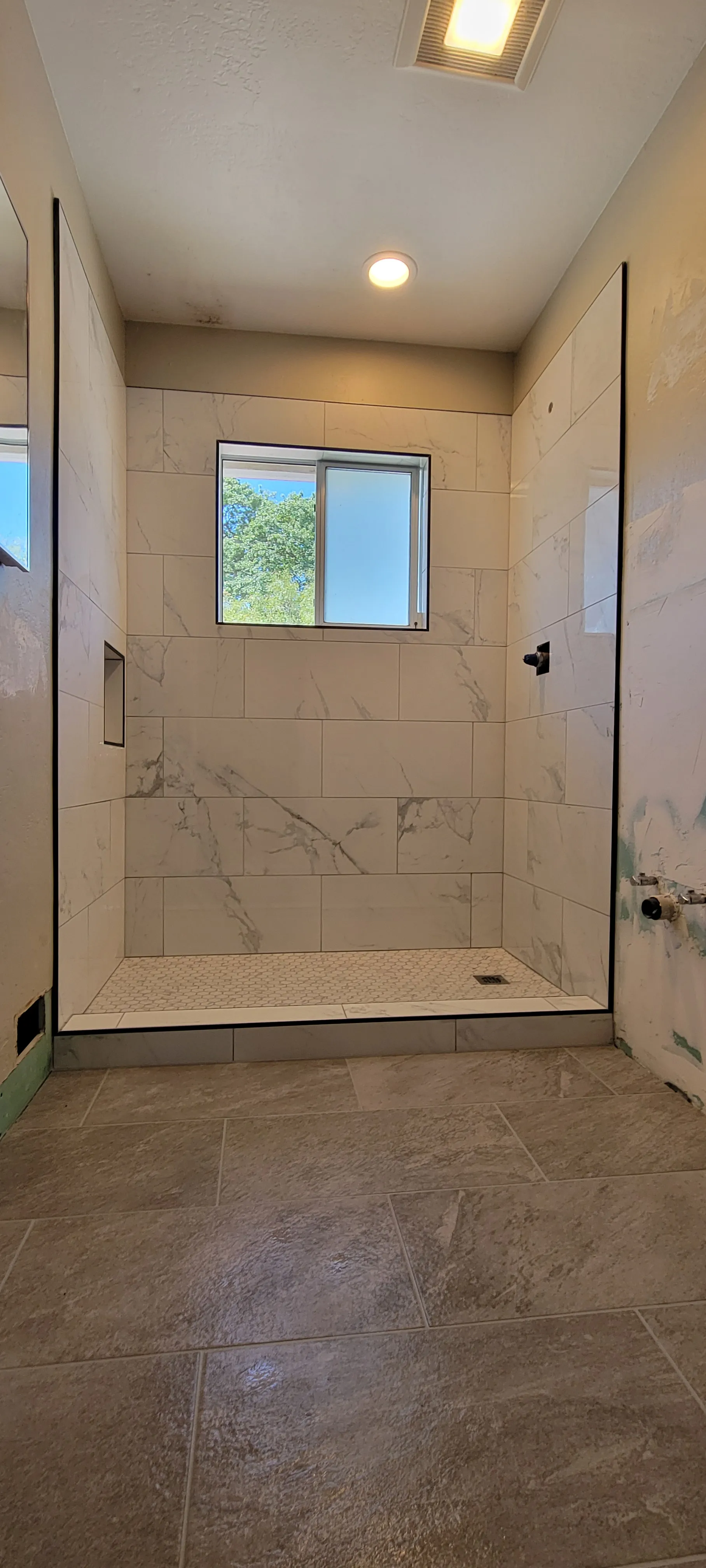 Narrow walk-in shower with large-format beige tiles, recessed lighting, and glass entry